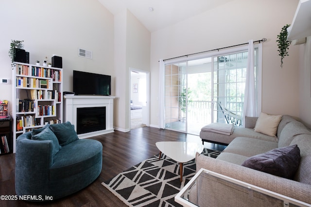 living area with dark wood-type flooring, visible vents, high vaulted ceiling, and a fireplace