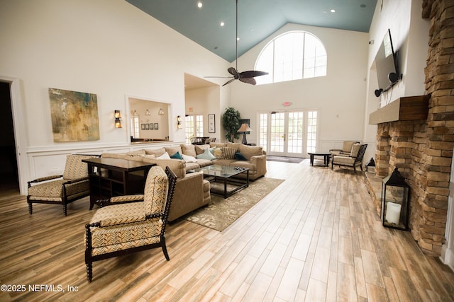 living area with a ceiling fan, wood finished floors, high vaulted ceiling, and a stone fireplace
