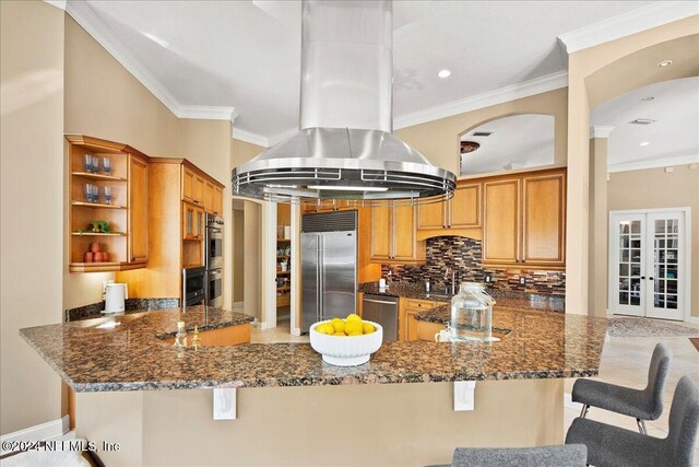 kitchen with dark stone countertops, open shelves, island range hood, stainless steel appliances, and a peninsula