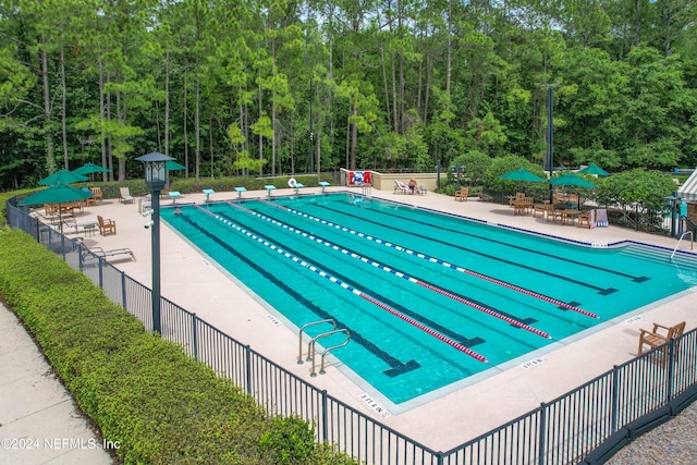 pool featuring a patio area, a forest view, and fence