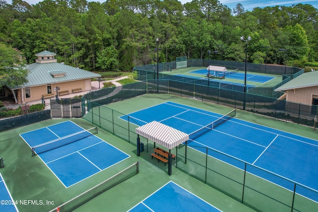 view of tennis court with a wooded view and fence