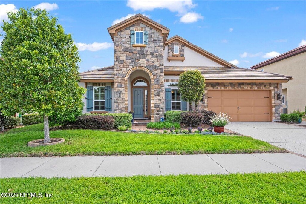 3781 Catania Pl, Jacksonville, FL 32224 - view of front facade with driveway, stone siding, stucco siding, a front lawn, and a garage
