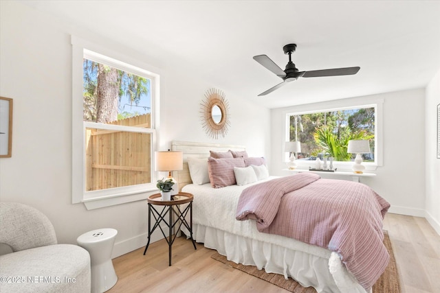 bedroom with ceiling fan, wood finished floors, baseboards, and multiple windows
