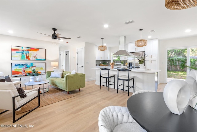 living room featuring a ceiling fan, visible vents, light wood finished floors, and recessed lighting