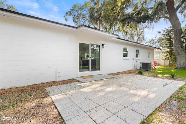 back of property with central AC, fence, concrete block siding, and a patio area