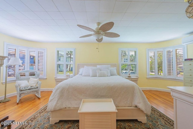 bedroom with wood finished floors, baseboards, a ceiling fan, and an AC wall unit