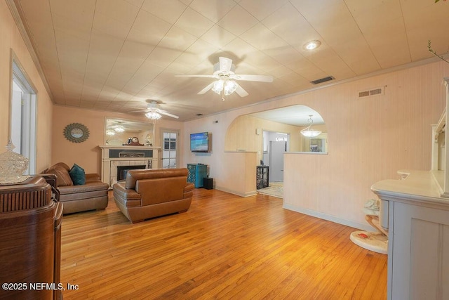 living area with arched walkways, light wood-style floors, ceiling fan, a tile fireplace, and ornamental molding