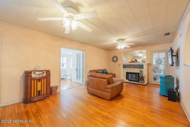 living room featuring light wood-style flooring, ceiling fan, a fireplace, healthy amount of natural light, and ornamental molding