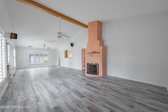 unfurnished living room featuring beamed ceiling, ceiling fan, wood finished floors, a fireplace, and high vaulted ceiling
