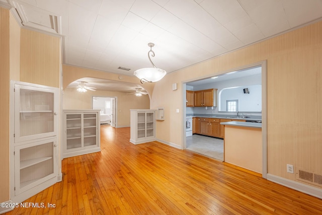 unfurnished living room with light wood-style flooring, plenty of natural light, a sink, and a ceiling fan