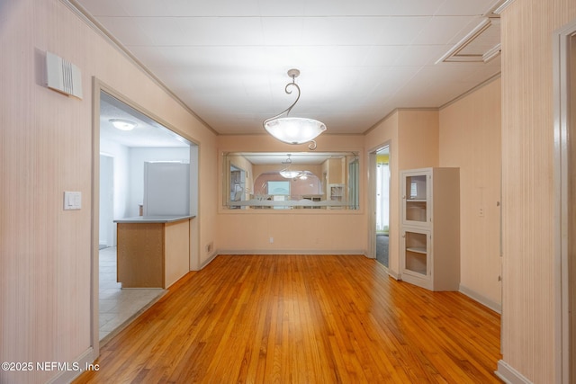 unfurnished dining area featuring light wood finished floors, crown molding, and baseboards