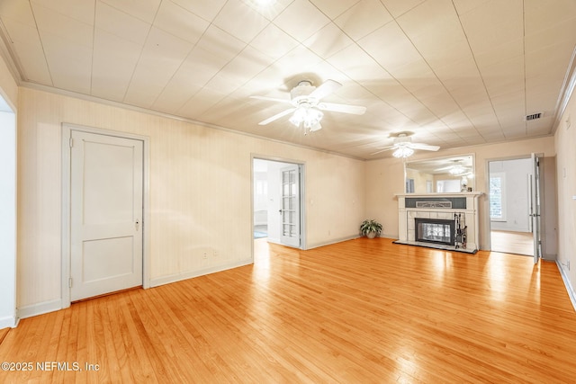 unfurnished living room featuring a ceiling fan, light wood-style floors, crown molding, a tiled fireplace, and baseboards