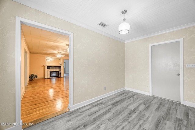 empty room featuring wood finished floors, a ceiling fan, ornamental molding, a tile fireplace, and baseboards