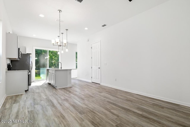 kitchen featuring visible vents, a center island with sink, a sink, a notable chandelier, and light wood-style flooring