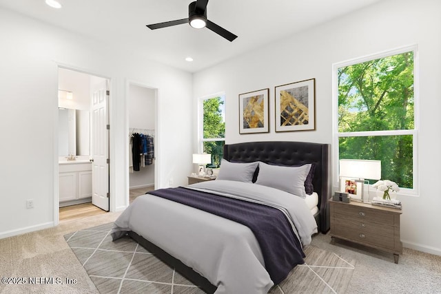 bedroom featuring connected bathroom, light colored carpet, a sink, baseboards, and a spacious closet