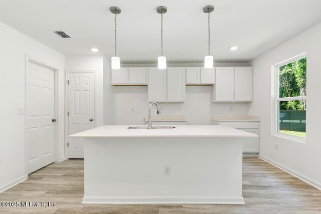 kitchen with light wood-style floors, an island with sink, white cabinetry, and a sink