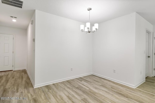 spare room featuring a notable chandelier, visible vents, and light wood-type flooring