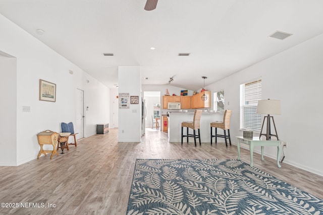 living room with visible vents, vaulted ceiling, baseboards, and light wood-style floors