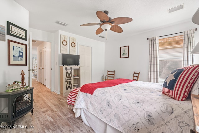 bedroom with a wood stove, wood finished floors, and visible vents