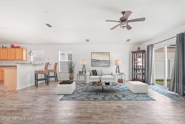 living area with a ceiling fan, visible vents, light wood-style flooring, and baseboards