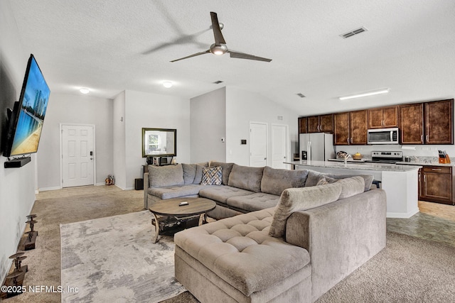 living room with a textured ceiling, visible vents, ceiling fan, and light colored carpet
