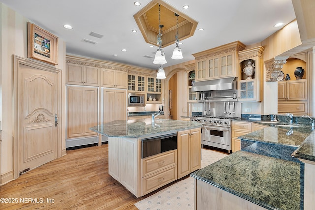 kitchen featuring stainless steel appliances, open shelves, under cabinet range hood, dark stone counters, and a kitchen island with sink