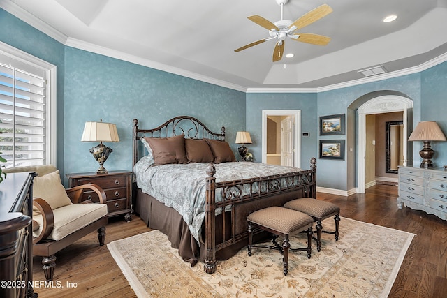 bedroom featuring wood finished floors, arched walkways, wallpapered walls, baseboards, and a ceiling fan