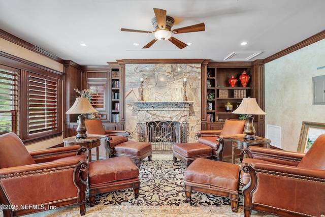 living room featuring ceiling fan, crown molding, built in shelves, recessed lighting, and a stone fireplace