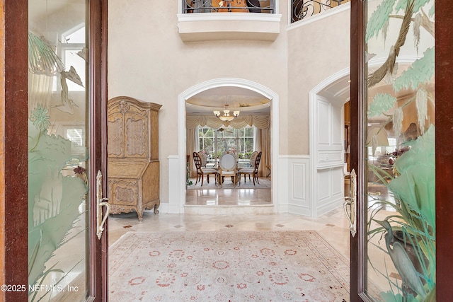entryway with a chandelier, arched walkways, wainscoting, a decorative wall, and a high ceiling