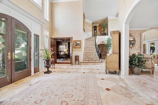 foyer entrance featuring arched walkways, plenty of natural light, a high ceiling, ornamental molding, and french doors