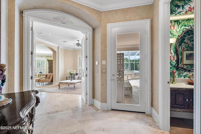 doorway with ornamental molding, healthy amount of natural light, baseboards, arched walkways, and a ceiling fan