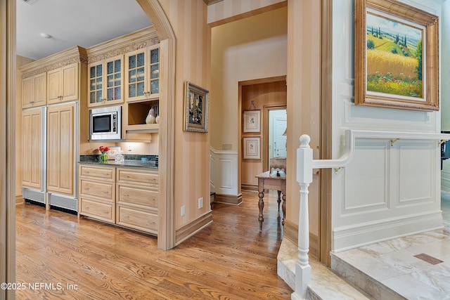 hallway featuring a decorative wall, light wood-style flooring, arched walkways, and a wainscoted wall