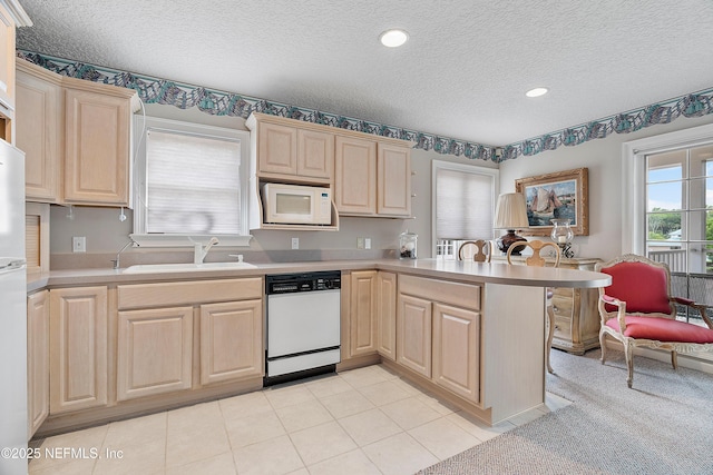 kitchen with white appliances, light brown cabinets, a peninsula, a textured ceiling, and a sink
