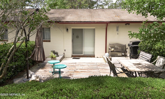 rear view of property featuring a shingled roof, concrete block siding, and a wooden deck