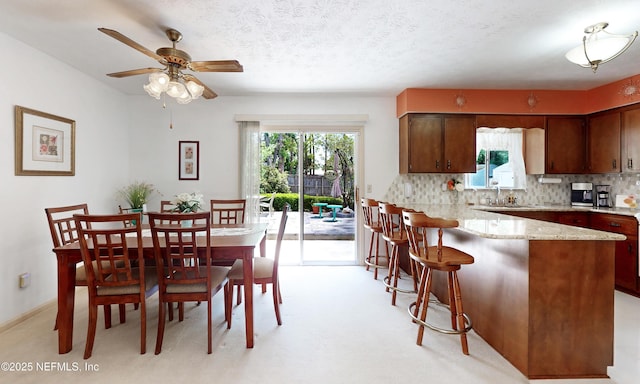 interior space featuring a peninsula, light stone countertops, ceiling fan, a kitchen bar, and tasteful backsplash