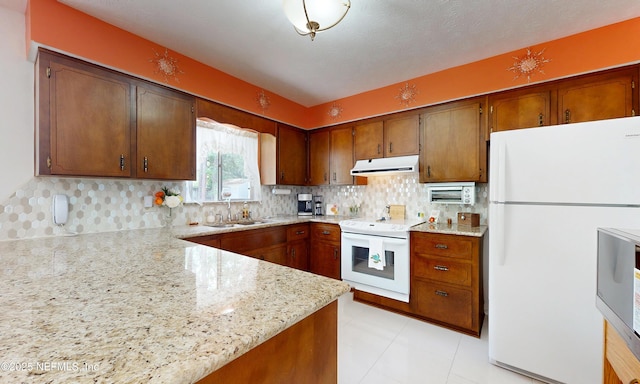 kitchen featuring decorative backsplash, white appliances, light stone countertops, under cabinet range hood, and a sink