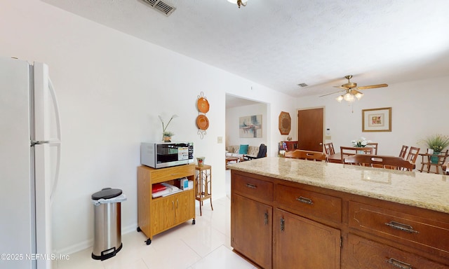kitchen featuring light tile patterned flooring, brown cabinetry, freestanding refrigerator, a ceiling fan, and visible vents
