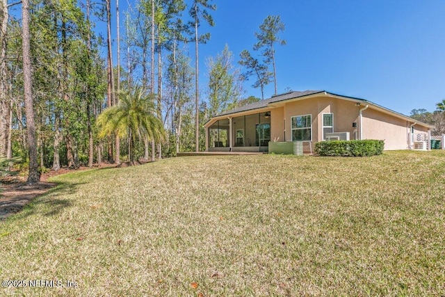 back of house featuring a sunroom, stucco siding, and a yard