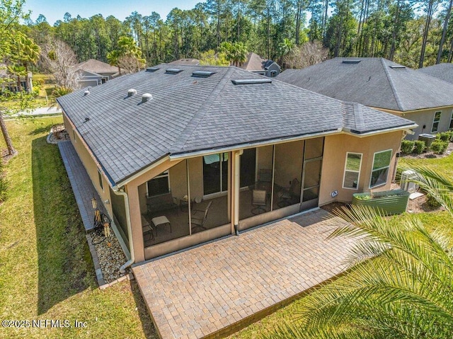back of house featuring a patio, roof with shingles, stucco siding, a sunroom, and a yard