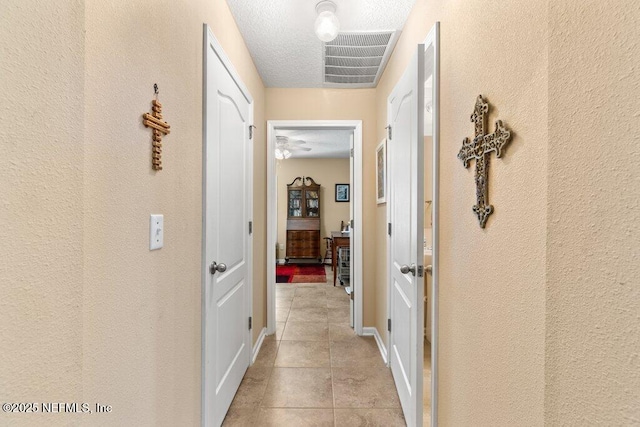 hall featuring light tile patterned floors, a textured wall, a textured ceiling, and visible vents