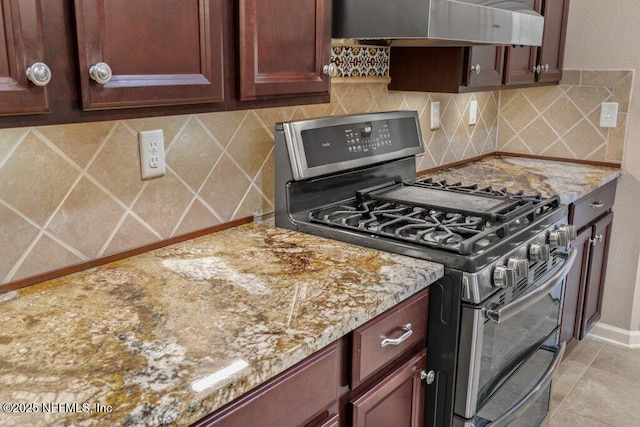 kitchen with backsplash, range with two ovens, light stone countertops, and wall chimney exhaust hood