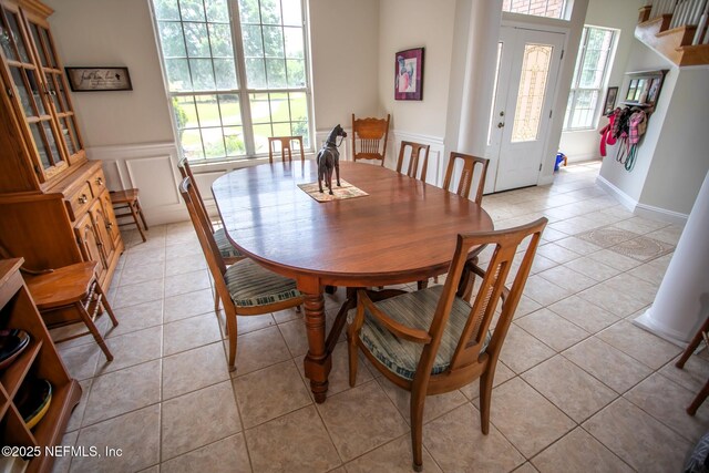 dining area with a decorative wall, wainscoting, light tile patterned flooring, and plenty of natural light