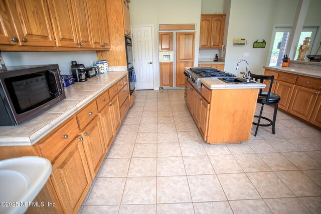 kitchen featuring light tile patterned floors, stainless steel appliances, a center island with sink, and a sink