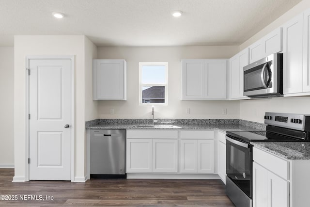 kitchen with white cabinets, light stone counters, a sink, appliances with stainless steel finishes, and dark wood-style flooring