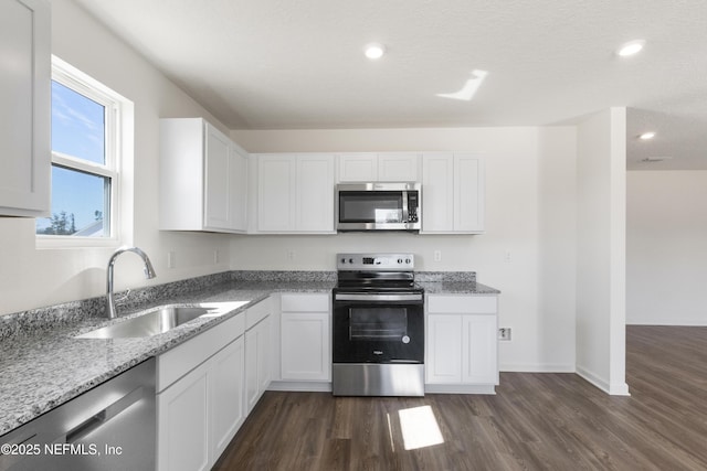kitchen featuring light stone counters, a sink, appliances with stainless steel finishes, white cabinets, and dark wood-style flooring