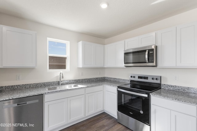 kitchen featuring white cabinets, dark wood finished floors, stainless steel appliances, a sink, and light stone countertops