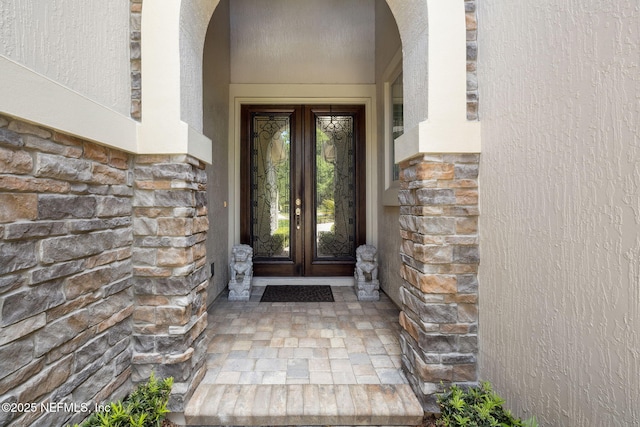 entrance to property featuring stucco siding, french doors, and stone siding