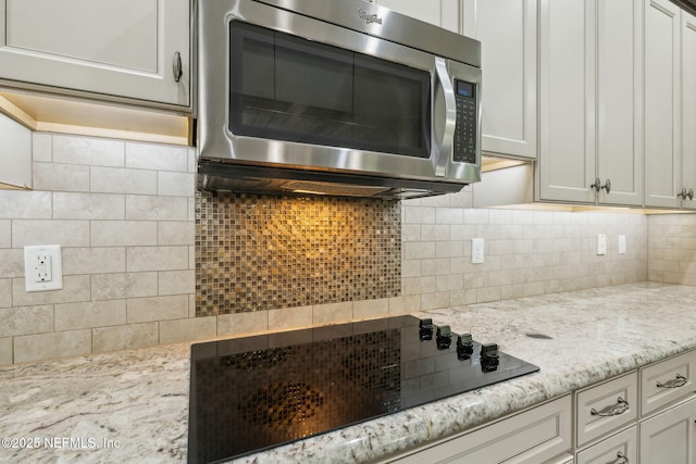 interior space with decorative backsplash, stainless steel microwave, and black electric cooktop