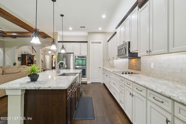 kitchen featuring a sink, open floor plan, dark wood-type flooring, arched walkways, and stainless steel appliances