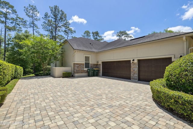 view of front of house with a garage, stucco siding, decorative driveway, and stone siding